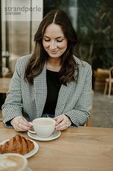 Woman enjoying coffee at a cafe with a croissant.