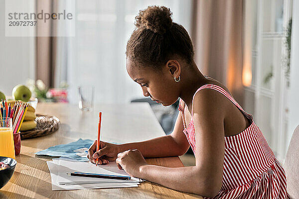 Afro kid girl doing homework or drawing in kitchen on breakfast