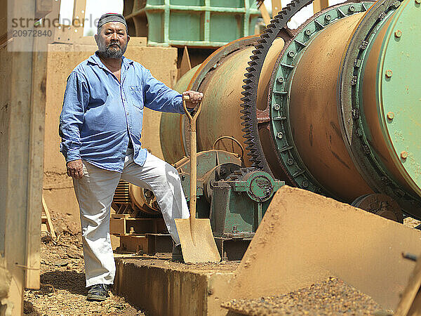 A project manager on a tin mining operation in Johor  Malaysia standing proudly next to heavy machinery used in the extraction.