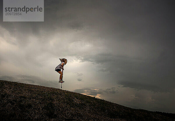 Young girl hopping down hill on pogo stick