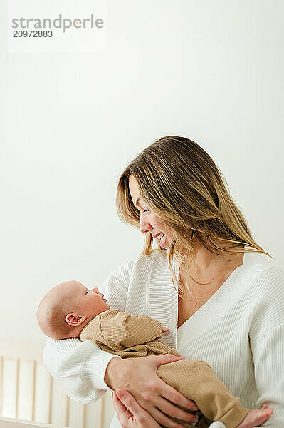 Mom smiles down at newborn baby with white background.