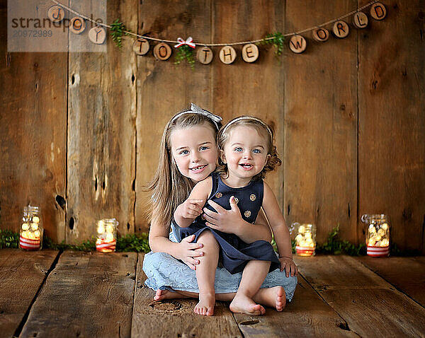 Beautiful young sisters hugging on wooden holiday backdrop