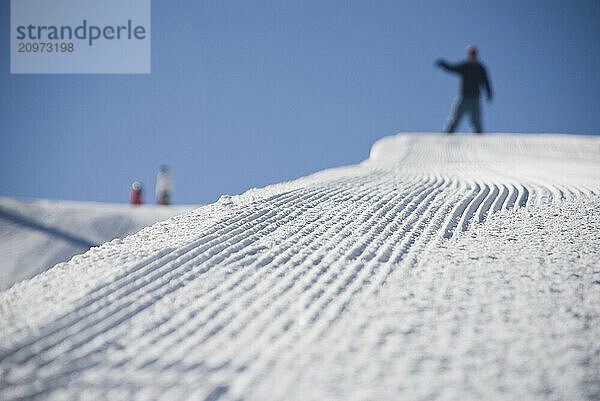 A half pipe deck perspective of a snowboarder signaling he's ready to drop in.