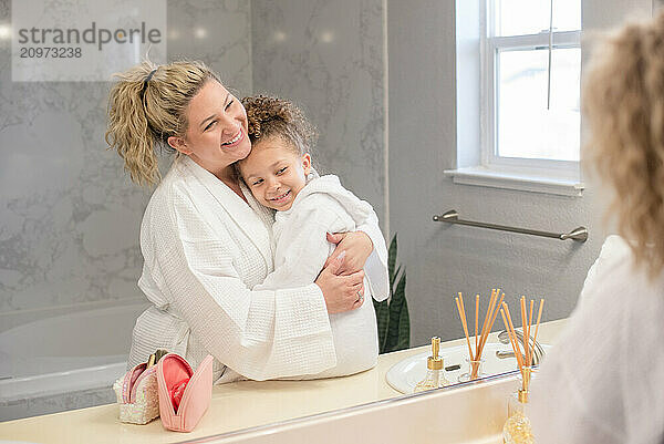 Mother hugging little daughter in the bathroom wearing white robes