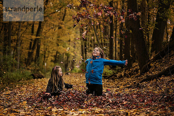 Happy young sisters playing in colorful leaf pile in fall