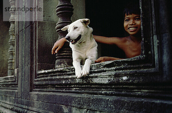 A boy and his pet dog sit happily at Angkor Wat Temple