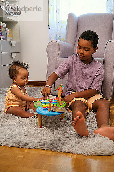 Older brother playing music with baby sister on colorful xylophone