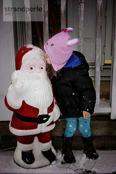 Young girl kissing Santa decoration outdoors