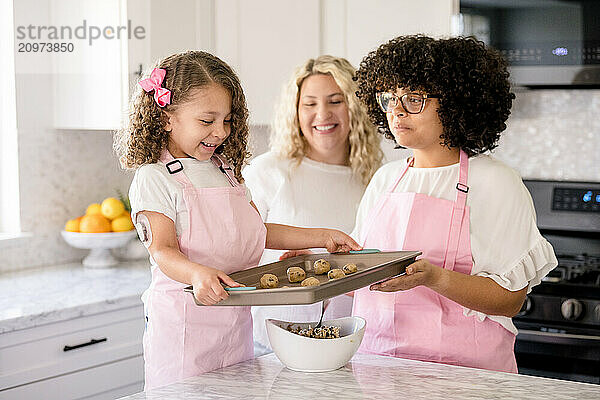 Little girl holding a baking sheet with cookie dough