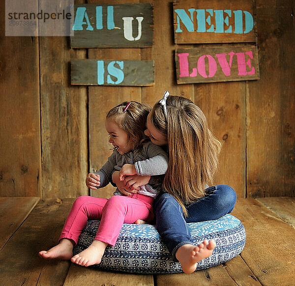 Young sisters laughing and playing indoors on weathered wood