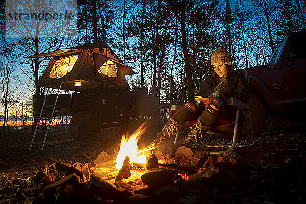 Young woman using smart phone by campfire  Biwabik  Minnesota  USA