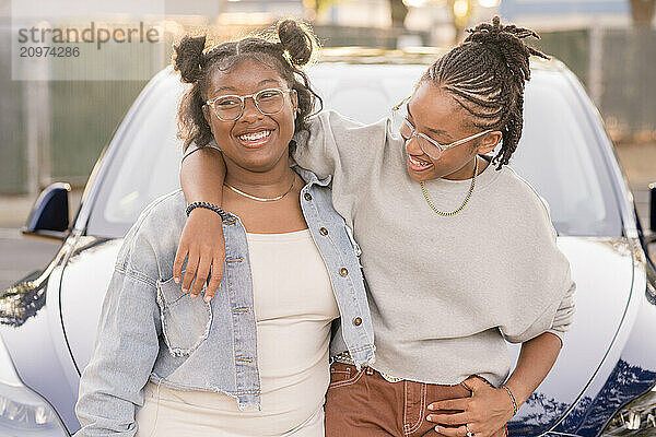 Young friends laughing together in front of car