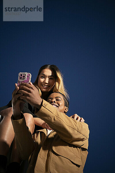 Multi racial couple taking a selfie at night against a deep blue