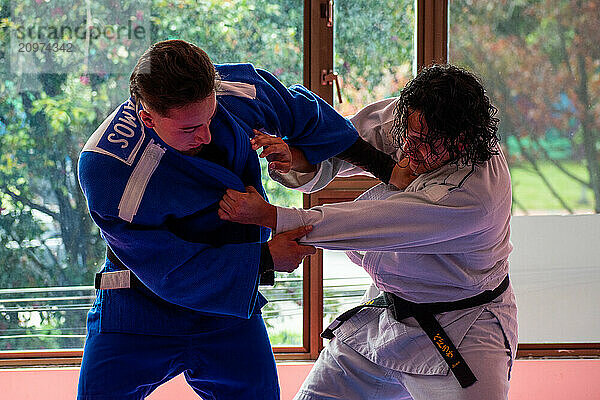 Judo fighters fighting in dojo with big windows at background