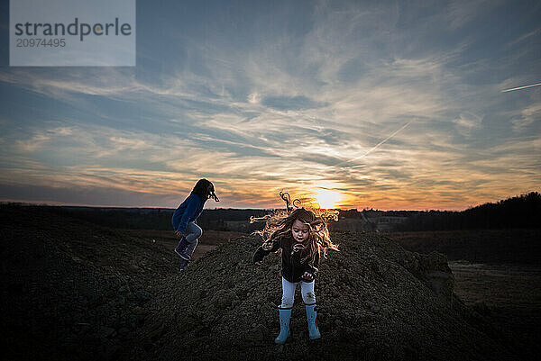 Young sisters playing on dirt pile at sunset