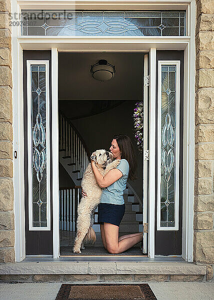 Woman hugging furry dog in front door after coming home.