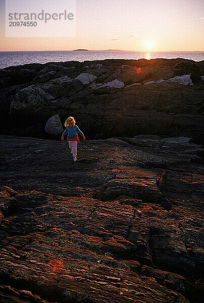 A young girl walks on the rocky beach of Hermit Island  Maine.