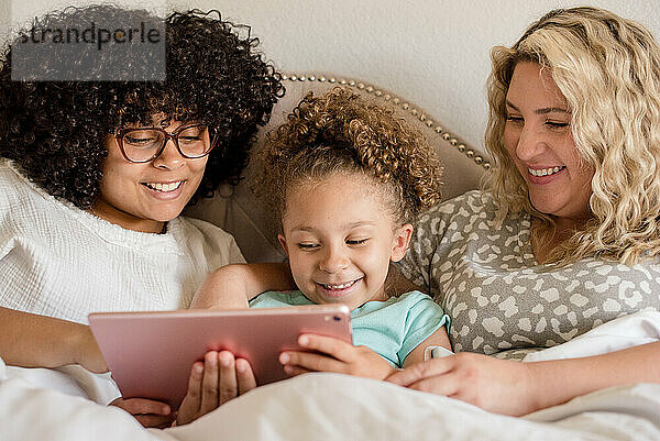 Mother and daughters smiling while looking at a tablet in bed