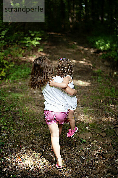 Big sister carrying young sibling down wooded path