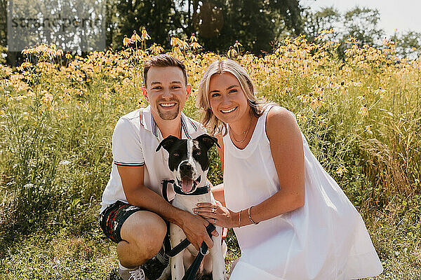 Smiling young couple with their dog in front of wildflowers