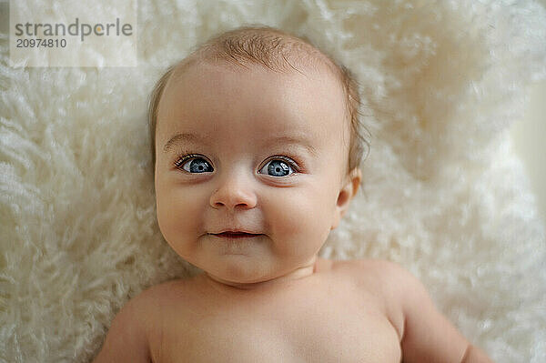 Portrait of beautiful baby big blue eyes smiling on white rug