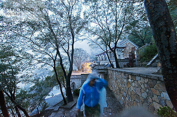 A poncho covered person walking in the rain at the San Huang Zhai Monastery on the Song Mountain  China.