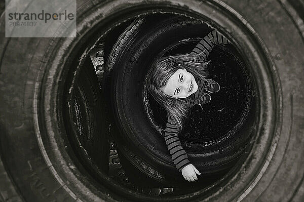 Young girl peeking through tires at outdoor playground