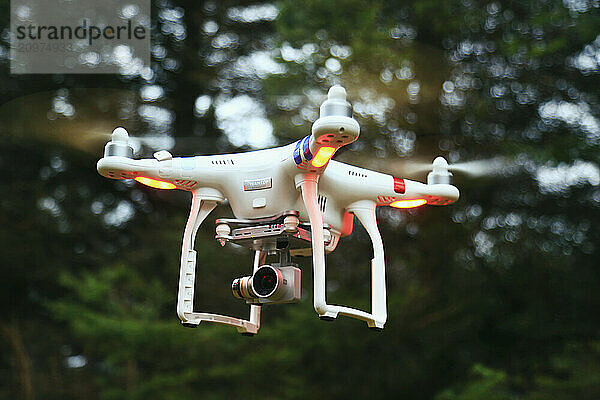 Drone hovering in mid-air against trees