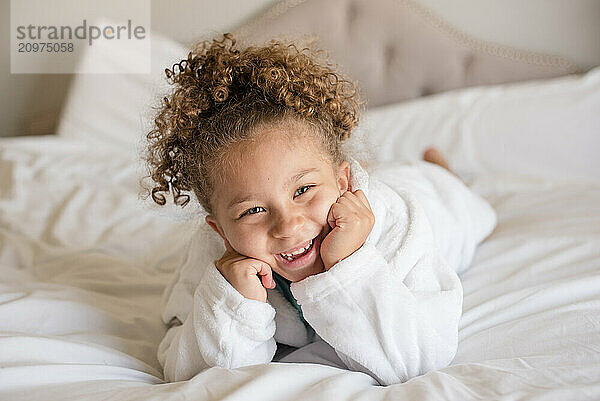 Biracial little girl is laying on her stomach in bed