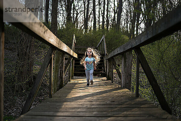 Young girl long blonde hair running down weathered bridge