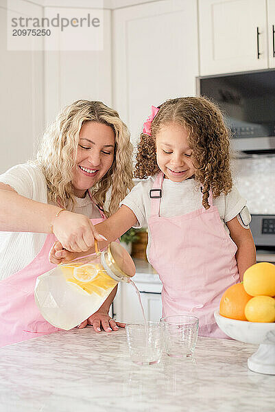 Mother helping daughter pour lemonade in glasses in the kitchen