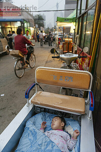 A baby left to sleep alone in the back of a motorcycle wagon