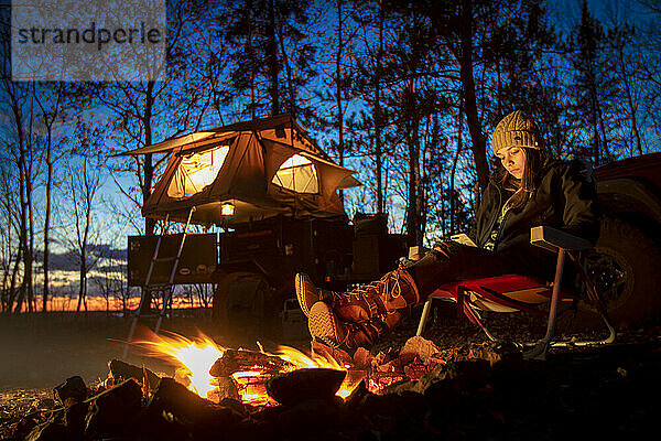 Young woman using smart phone by campfire  Biwabik  Minnesota  USA