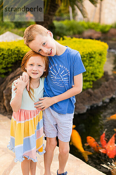 Brother and Sister hugging by koi pond