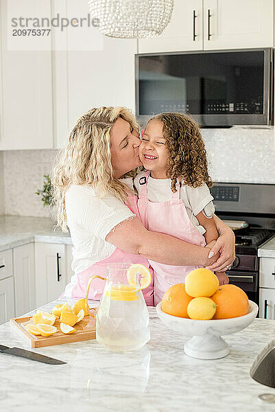 Mother giving little daughter a kiss in the kitchen with lemons