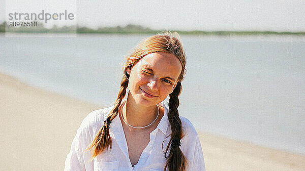 Girl winks playfully while on a beach  sea in the background.