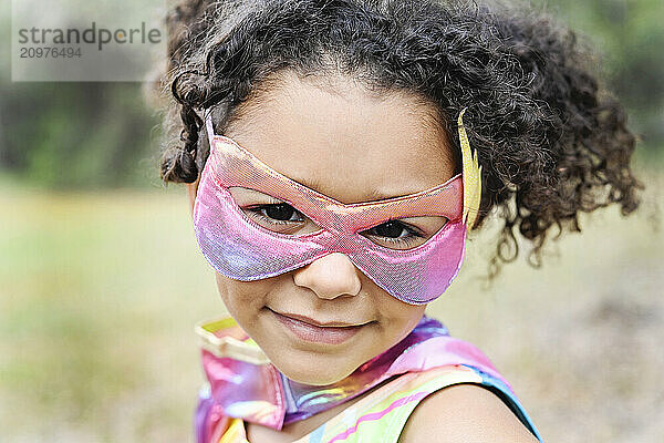 Close-up of a young girl in a superhero mask smiling  with curly