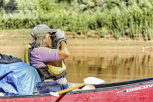 Elderly Woman looks through binoculars while canoeing on the Green River in Canyonlands National Park  Utah