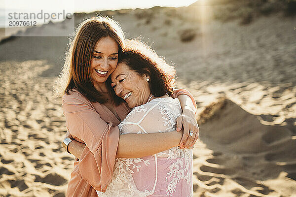 Woman hugging elderly mother happy smiling at beach at sunset