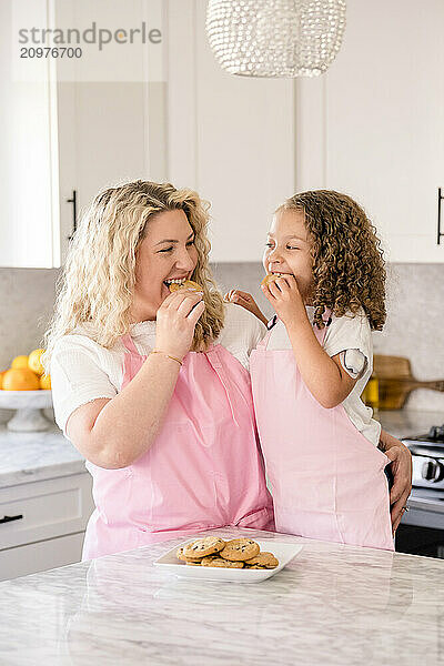 Mother and daughter eating a cookie in the kitchen together