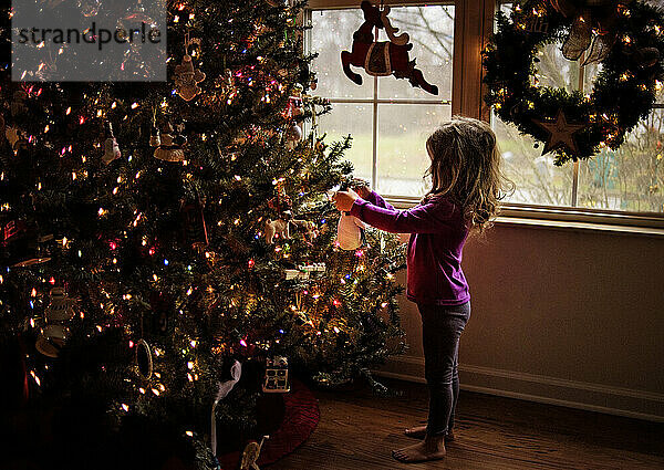 Toddler decorating colorful Christmas tree in front of window