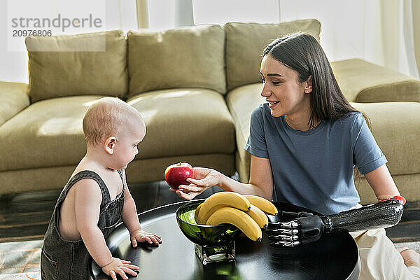 Young woman with prosthesis puts fruits with baby boy