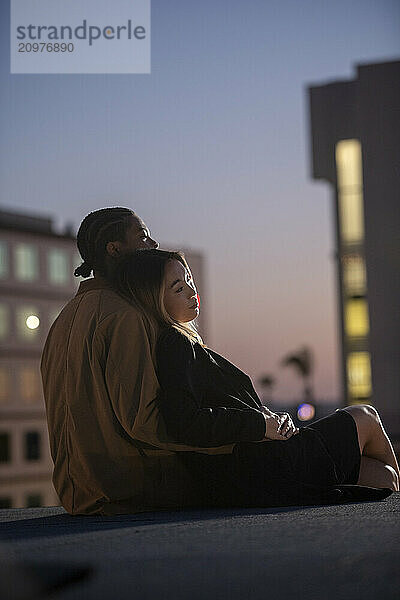 Multi racial couple relaxing and reclining in thought on rooftop