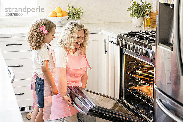 Mother holding the oven door open for daughter to see the cookies