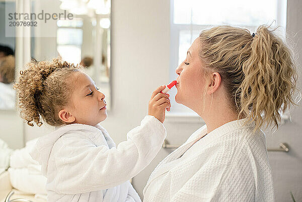 Little daughter is putting lipstick on mothers lips