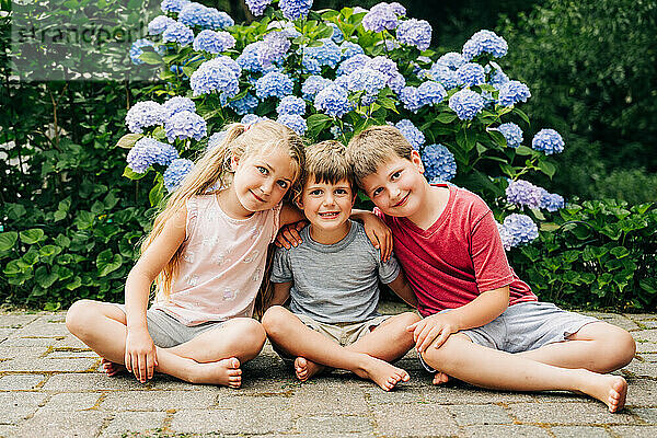 Three kids sitting together with blue hydrangeas in the background