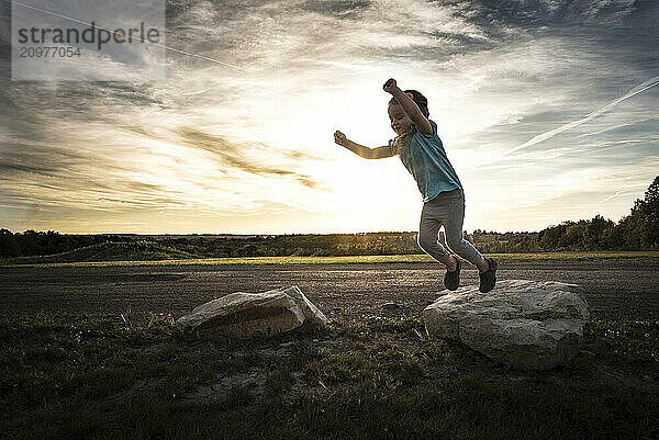 Little girl jumping off rocks at sunset