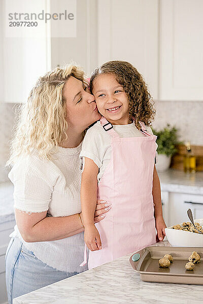 Mother giving daughter a kiss on the cheek in the kitchen