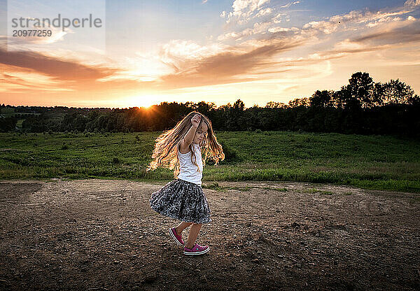 Little girl long blonde curls dancing at sunset