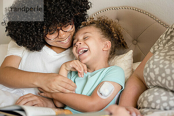 Little girl with glucose monitor laughing with her big sister in bed